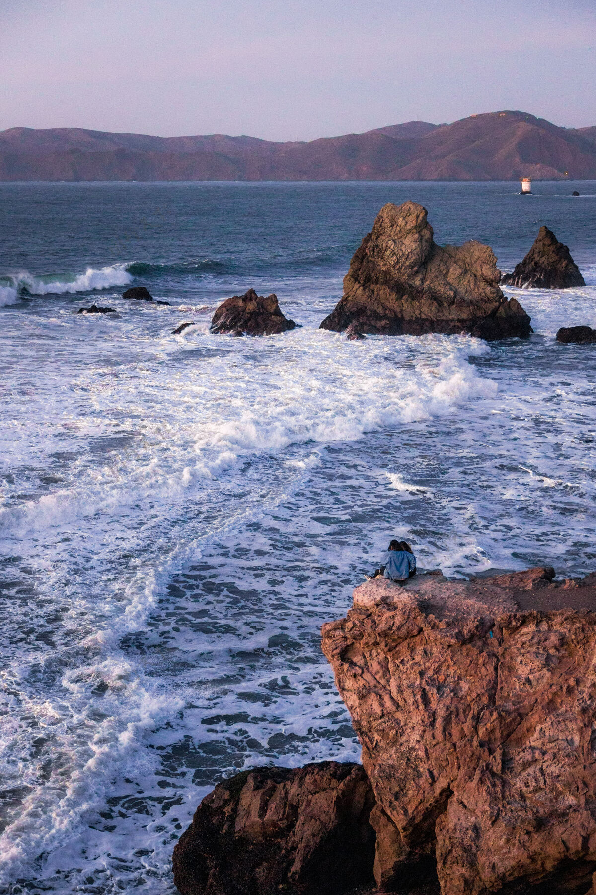 海洋一个穿着黑衬衫的人白天坐在海边的棕色岩石上海角自然人类