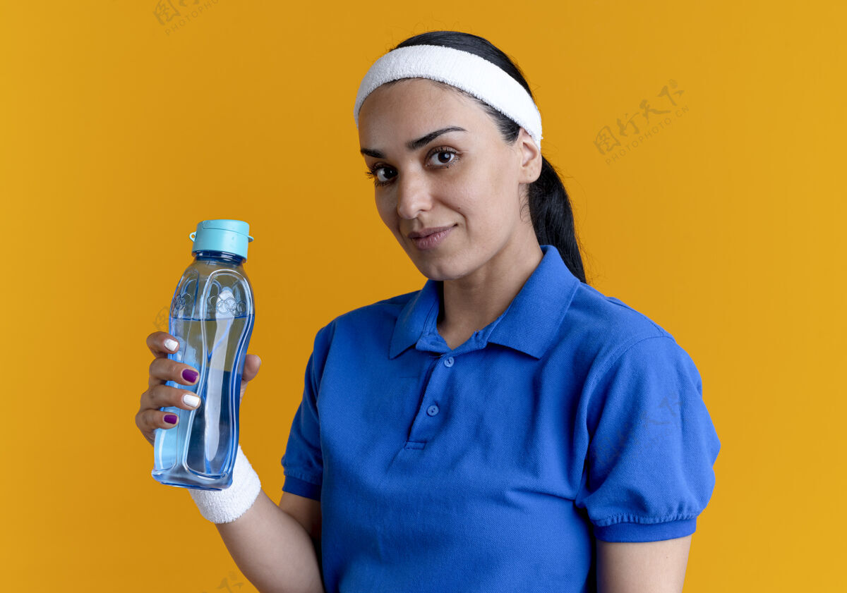 腕带年轻自信的白人运动女性戴着头带和腕带 拿着橙色的水铃 留着复制空间女人空间佩戴
