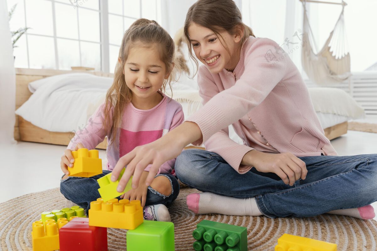 水平两个微笑姐妹在家玩玩具的正面图兄弟姐妹娱乐乐趣