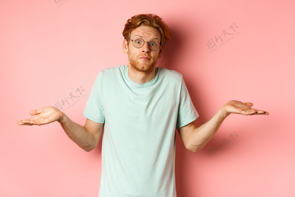 男人照片中的红发帅哥戴着眼镜 穿着t恤 什么都不知道 耸耸肩 扬起眉毛 茫然地站在粉色的背景下头发成人困惑