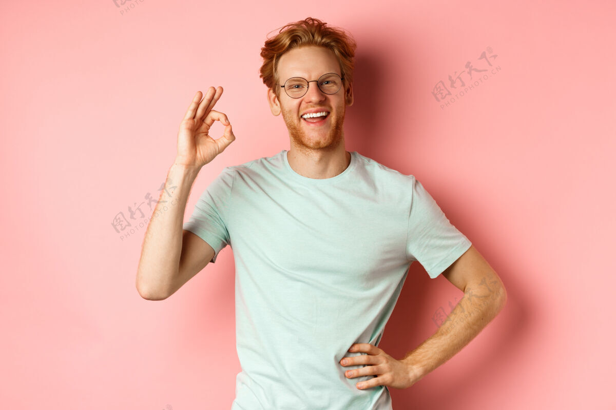 保证兴高采烈的家伙 红头发 红胡子 戴着眼镜 表示同意并说同意 微笑着满意 站在粉红色的背景上红发成人同意