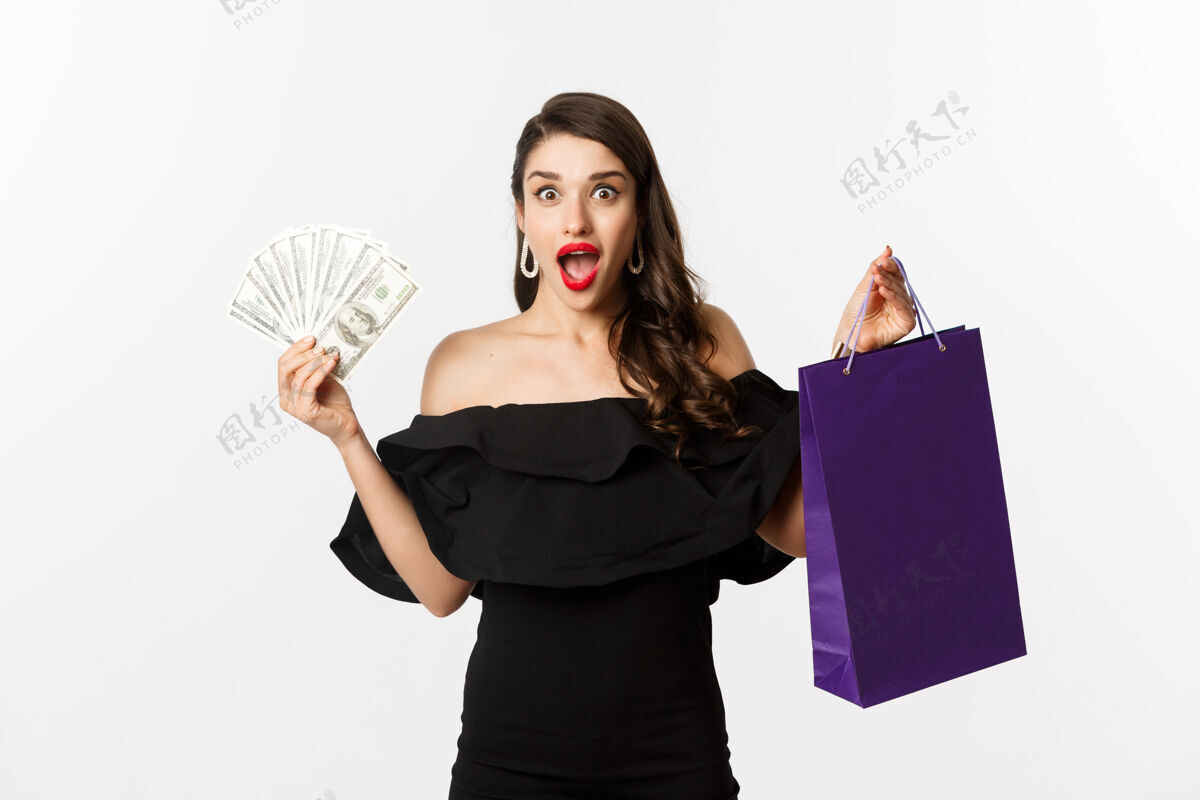 口红快乐的女买家拿着购物袋和钱 穿着黑色衣服站在白色背景上复制空间服饰金钱模型