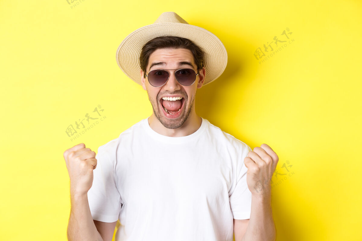 黄色旅游和度假的概念幸运的人旅游者赢得门票 做拳头泵和说是的 穿着度假服 站在黄色背景下夏天男人帽子