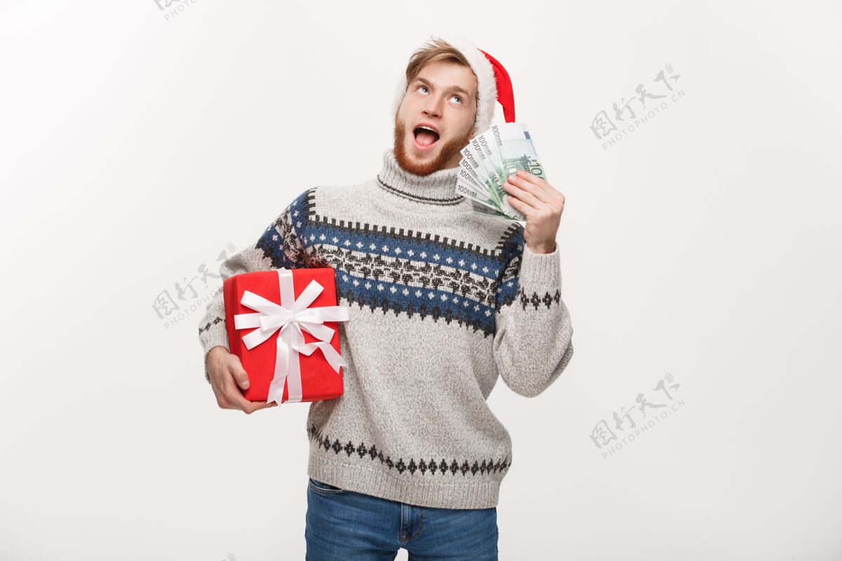 男性年轻的胡须男手里拿着圣诞礼盒和白色的钞票欢呼快乐手势