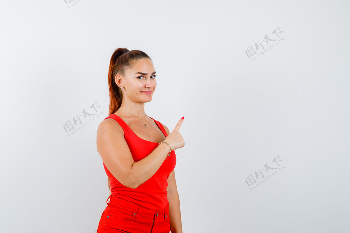 女性美丽的年轻女子的肖像指向右上角在红色背心 裤子和看起来自信的前视图专业裤子休闲