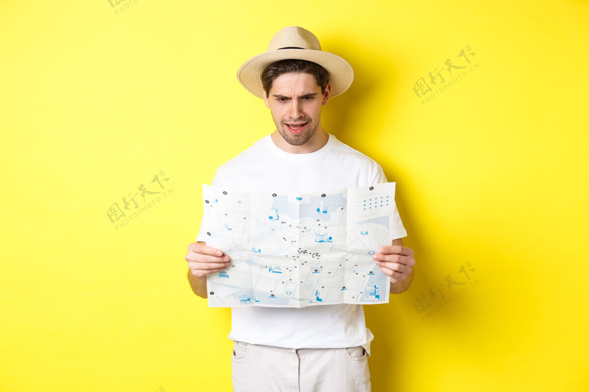 地图旅游 度假和旅游的概念男人在旅途中看不清地图 看不懂 站在黄色背景上自信帽子假日