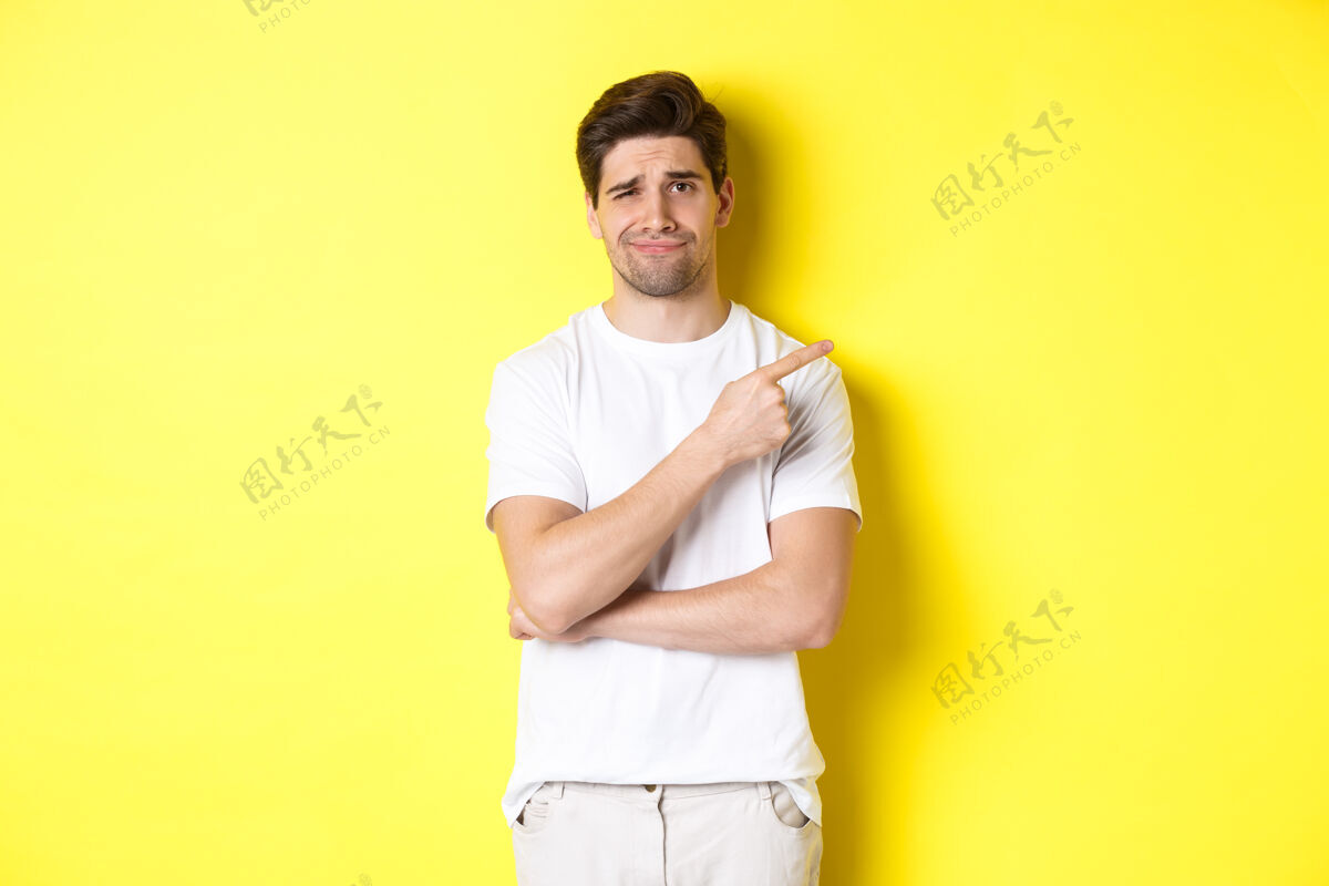 站一个多疑而不安的人用手指着一个瘸子 不情愿地皱着眉头 站在黄色的背景上模特时尚表情