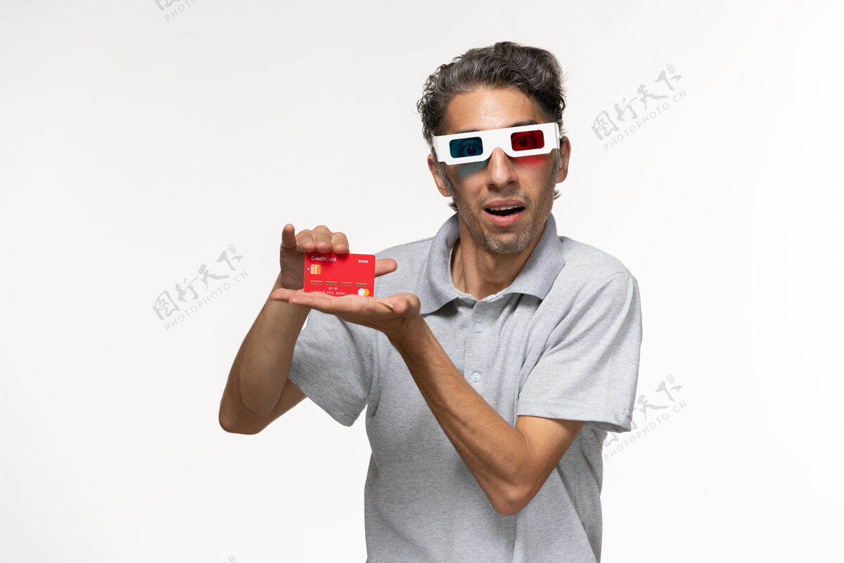 享受正面图：年轻男子戴着d墨镜 手持红色银行卡 坐在白色办公桌上男武器太阳镜