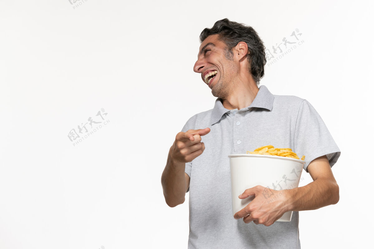 电影正面图：年轻的男性拿着一个篮子 里面放着薯片 和一个在白色表面上笑的人说话远程有人商人