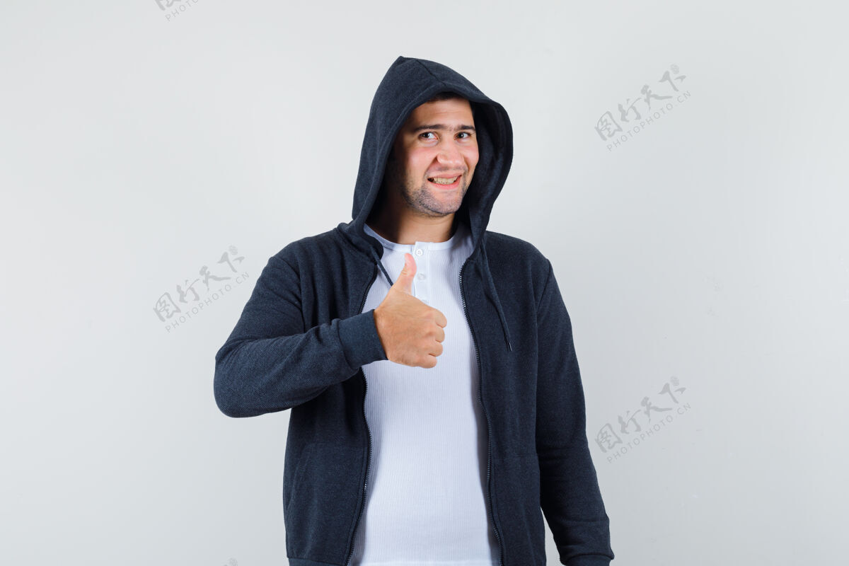 年轻年轻的男性穿着t恤衫 夹克衫竖起大拇指 看上去很快乐 正面视图前面休闲肖像