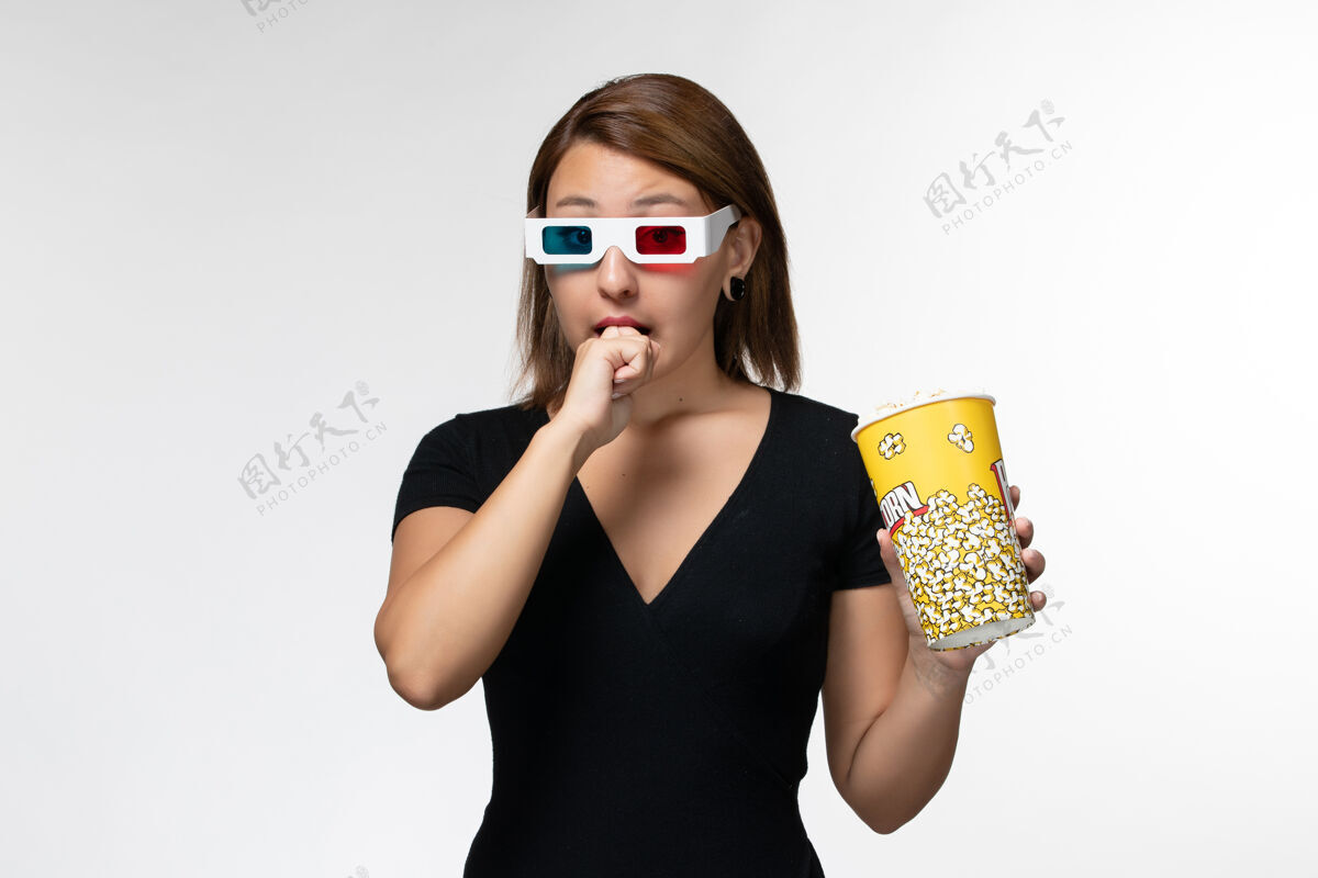 电影正面图戴着d型太阳镜拿着爆米花的年轻女性在白色表面看电影太阳镜爆米花前面