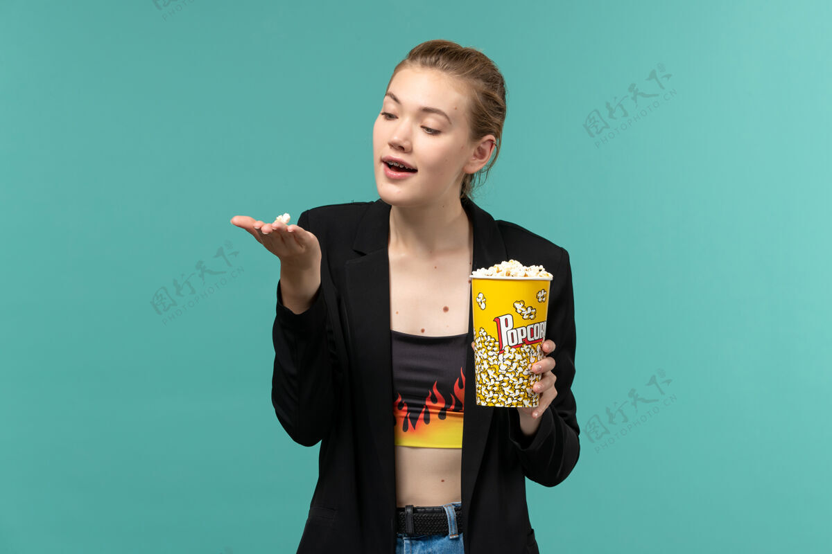剧院正面图：年轻的女性拿着爆米花在蓝色的桌子上看电影电影正面观看