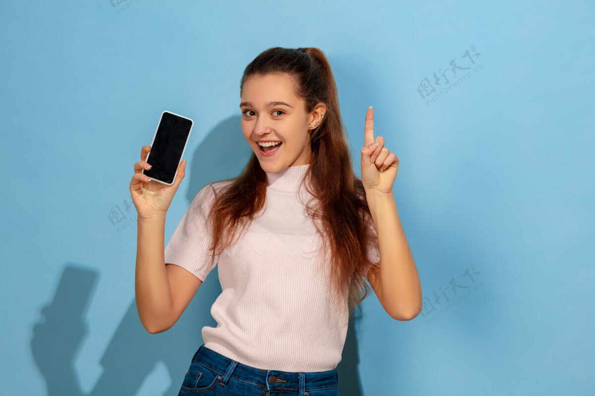 模特十几岁的女孩 指着手机屏幕衬衫学习快乐