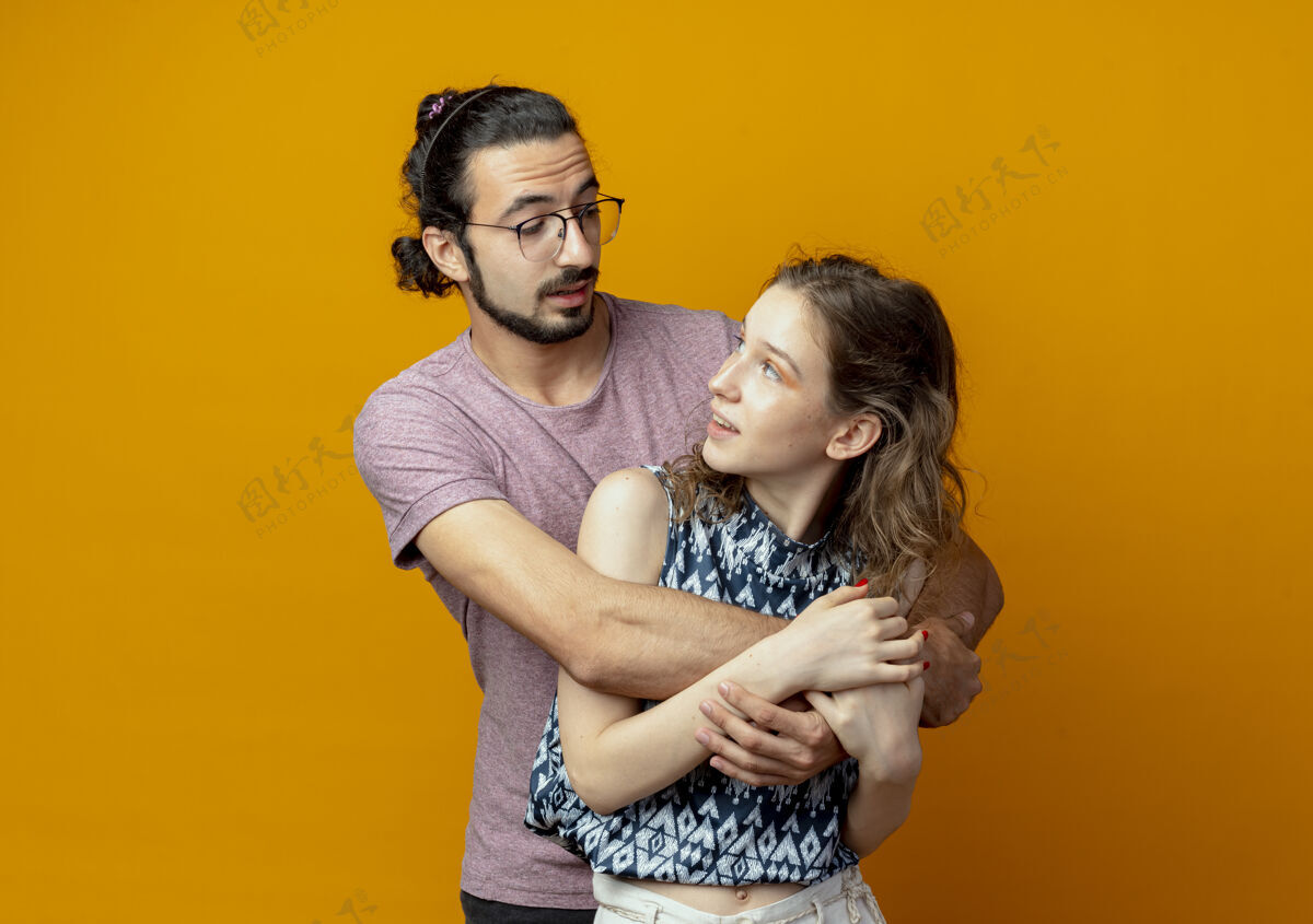 女人年轻漂亮的情侣男女在爱中幸福地拥抱在一起站在橘色的墙上夫妻拥抱年轻