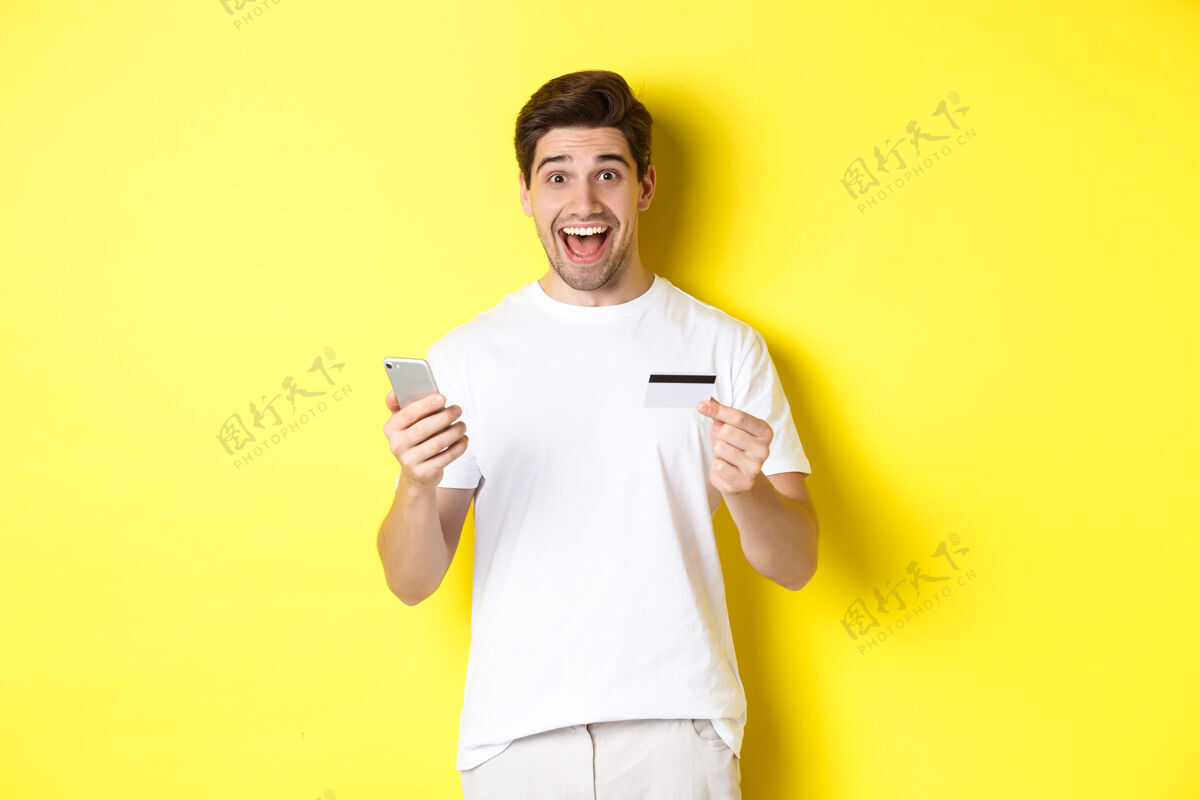 男人快乐男买家手持智能手机和信用卡 网上购物的概念 站在黄色背景下模特黄色帅哥
