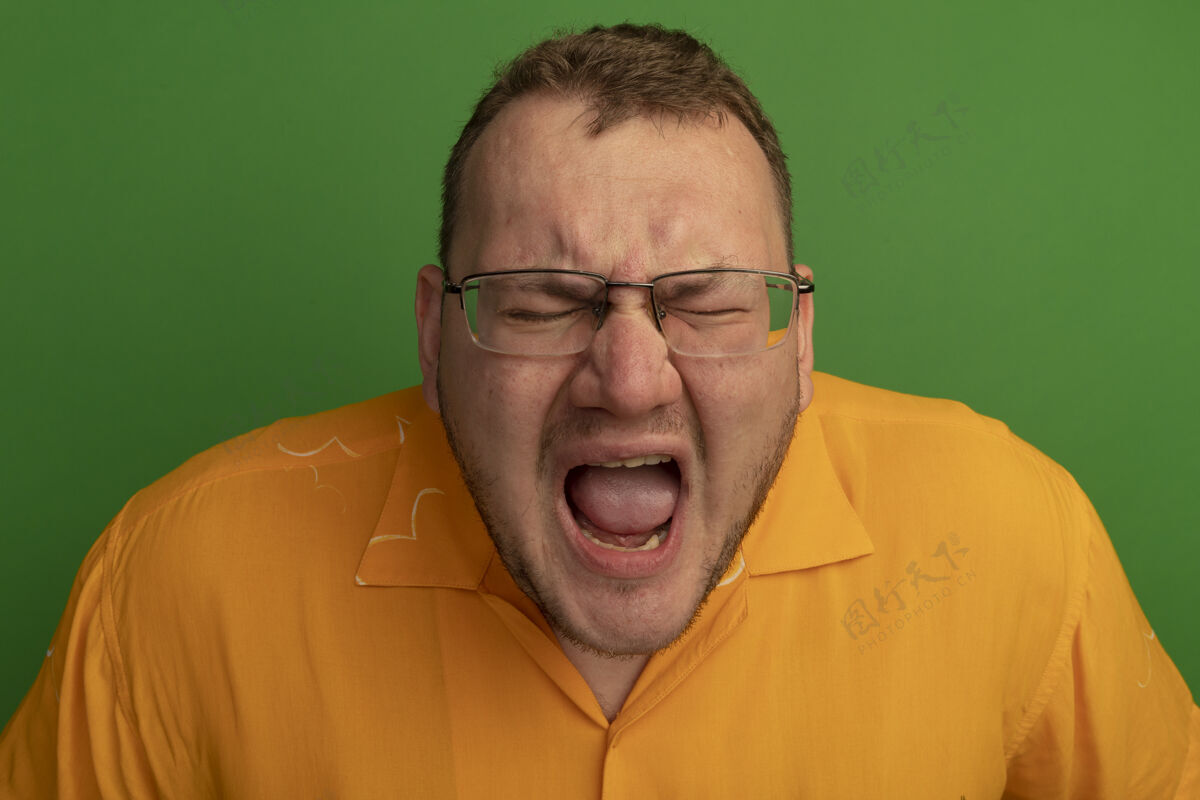 咄咄逼人一个戴着眼镜 穿着橙色衬衫的男人站在绿色的墙上 带着咄咄逼人的表情大喊大叫站着喊着表情