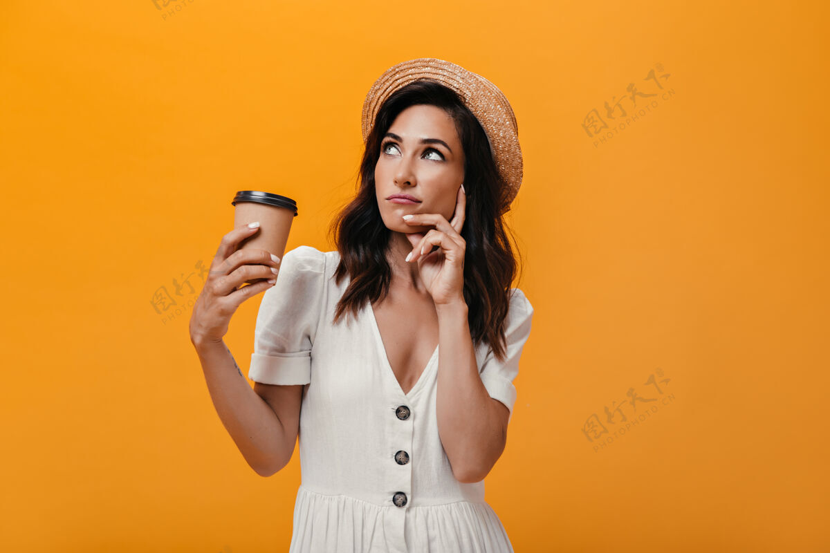 梦幻戴草帽的姑娘抬起头来 若有所思地端着一杯咖啡一个穿着白色夏装 手里拿着咖啡的沉思女人摆姿势裙子圆点室内
