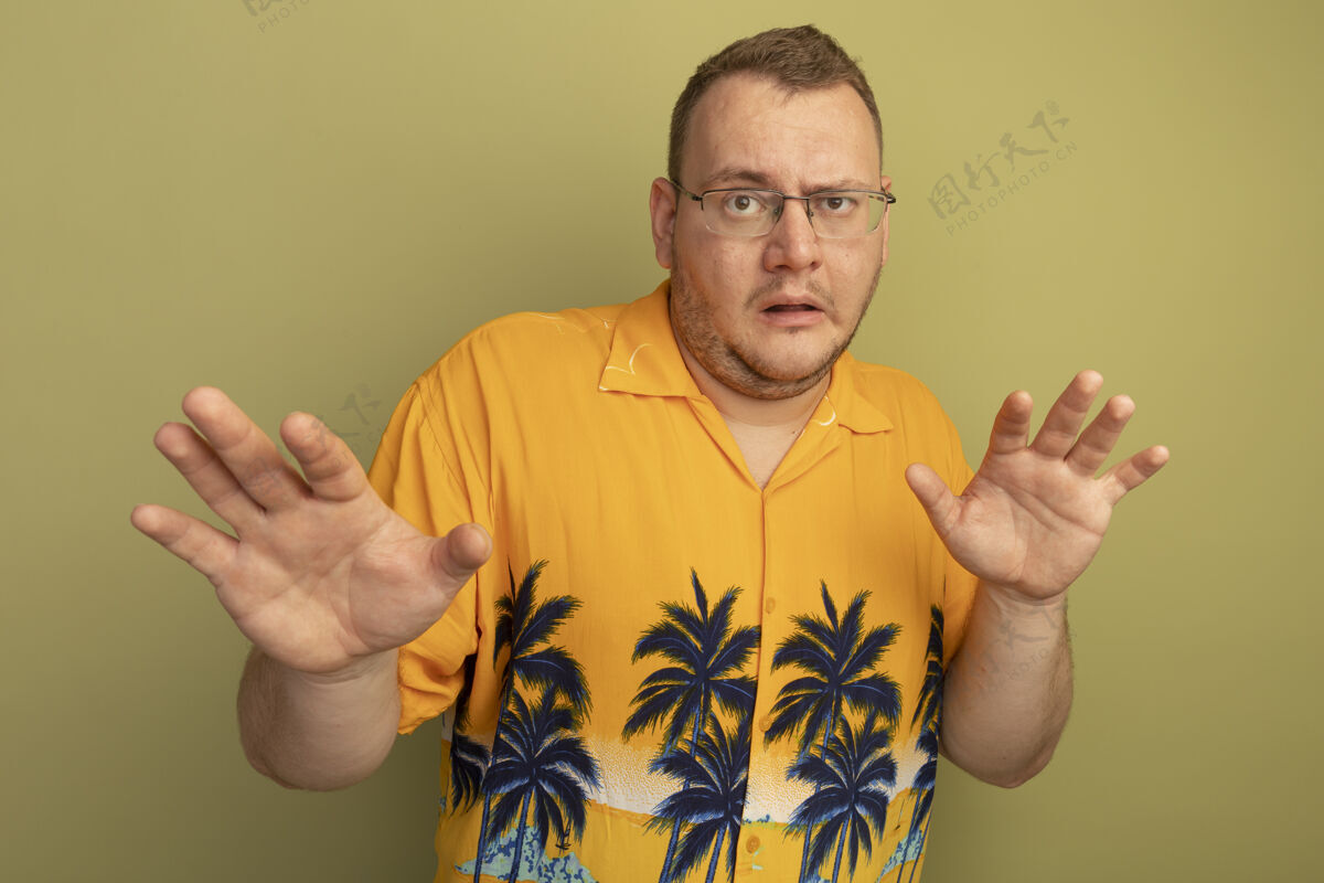 手臂一个戴着眼镜 穿着橙色衬衫的男人伸出双臂 站在绿色的墙上做着防御的手势防御制造站立
