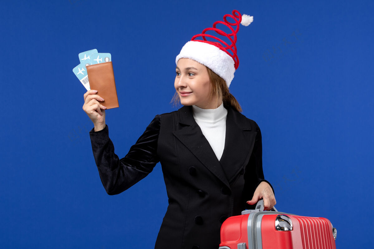 圣诞节正面图：年轻女性拿着票和包在蓝色办公桌上的女人度假度假举行视图工作