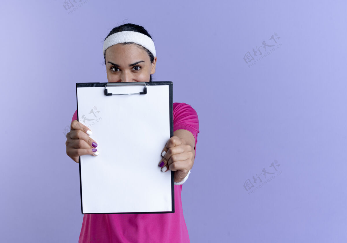剪贴板年轻快乐的白人运动女性戴着头带和腕带 在紫色的空间里拿着一个孤立的剪贴板年轻紫色太空