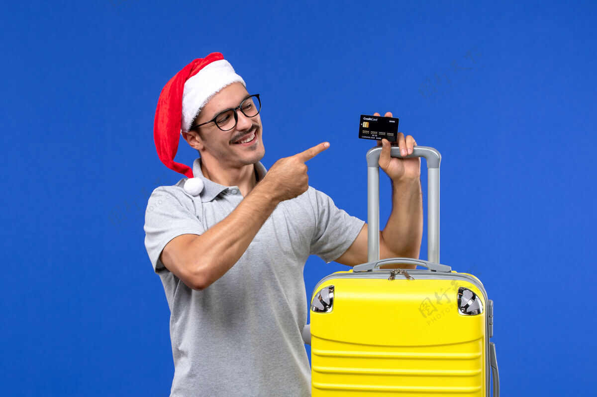 工程师正面图年轻男子手持黄包银行卡上蓝墙旅游情感度假持有圣诞节年轻男性