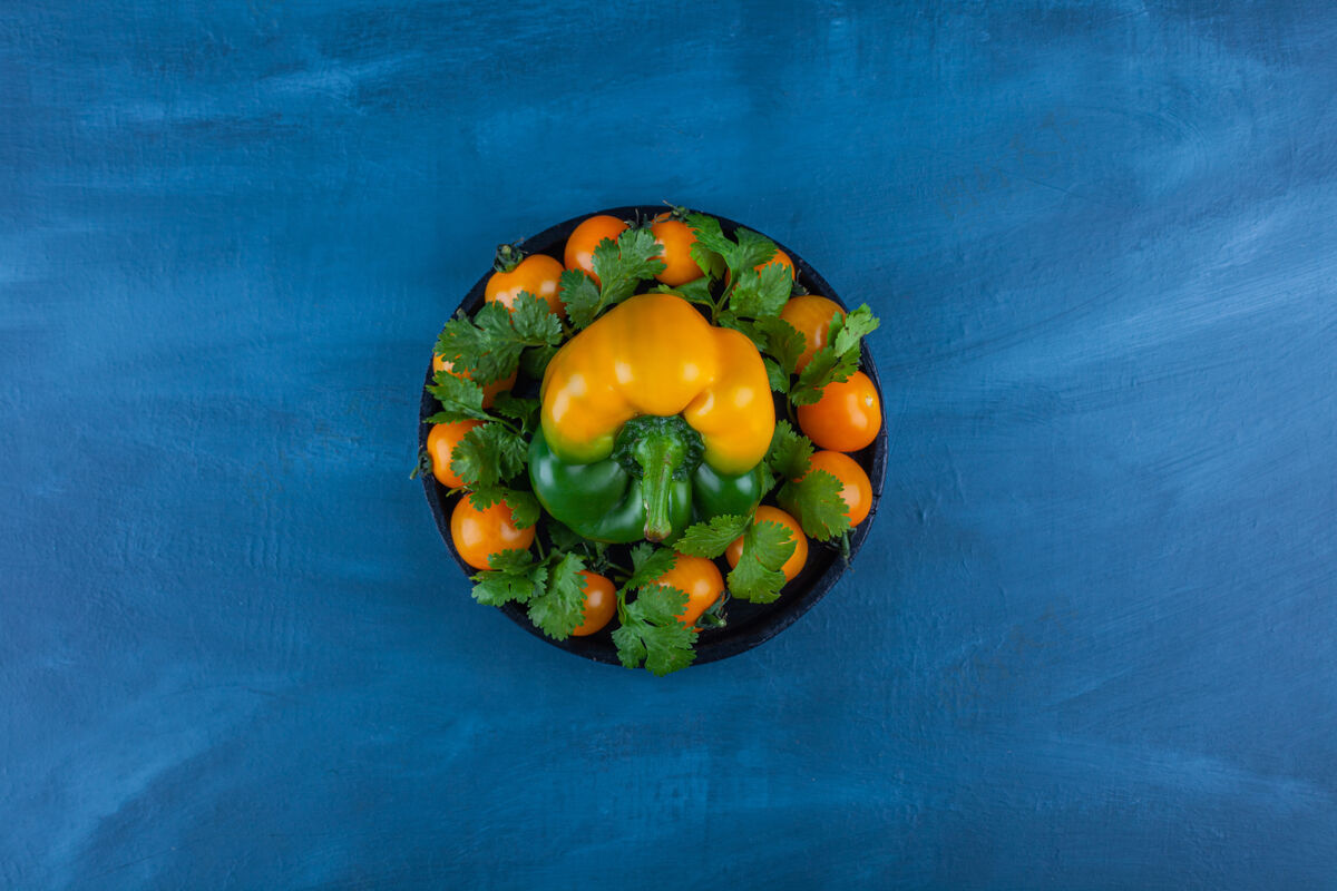 健康蓝色桌子上摆着一盘黑甜椒和樱桃番茄蔬菜成熟生的