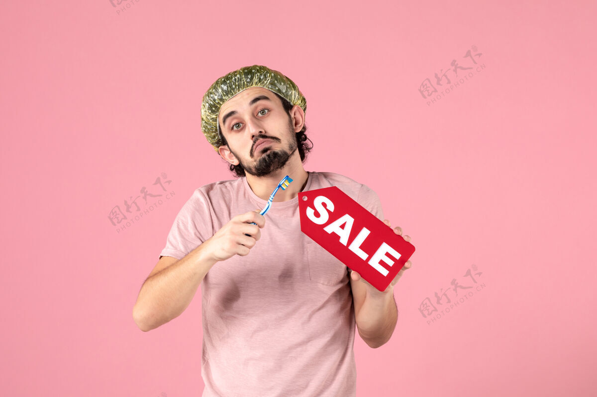 保湿正面图：手持牙刷的年轻男性 粉色背景上有销售铭牌微笑标签男人