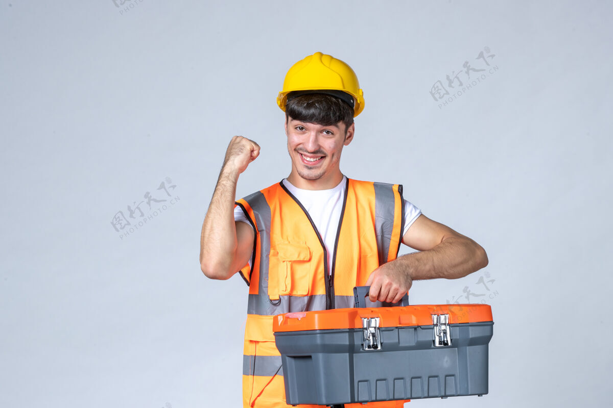 修理工正面图：年轻的男性工人拿着白色背景的工具箱工具头盔工作