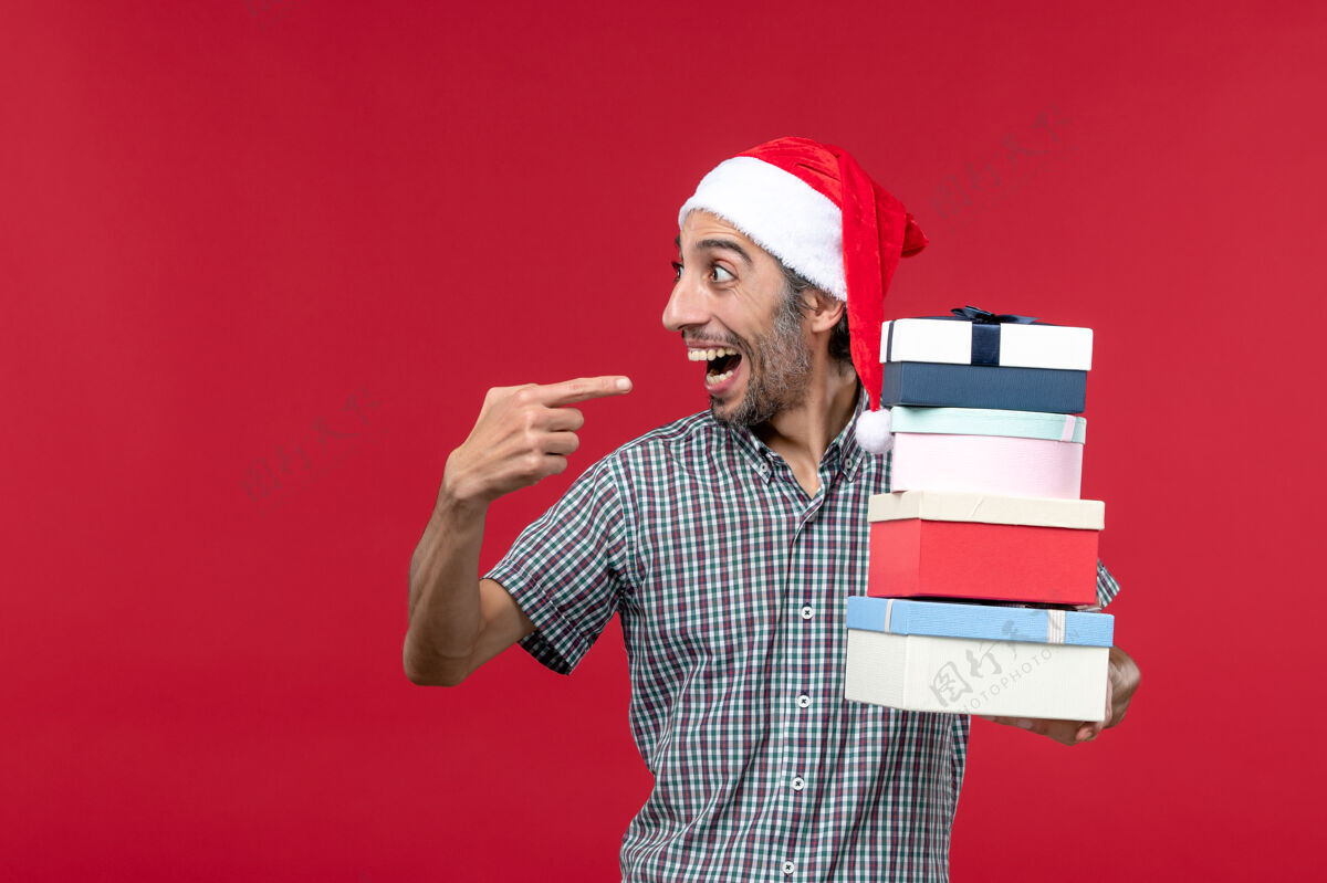 情绪正面图：年轻的男性高高兴兴地拿着红色背景上的礼物举行前面圣诞