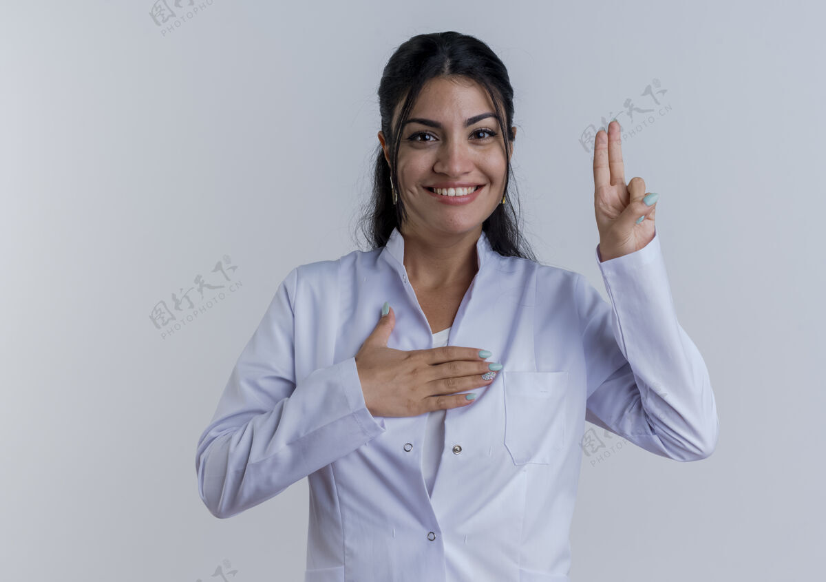 医疗面带微笑的年轻女医生穿着医用长袍做着承诺的手势 隔离在白色的墙上 留着复印空间微笑表情手势