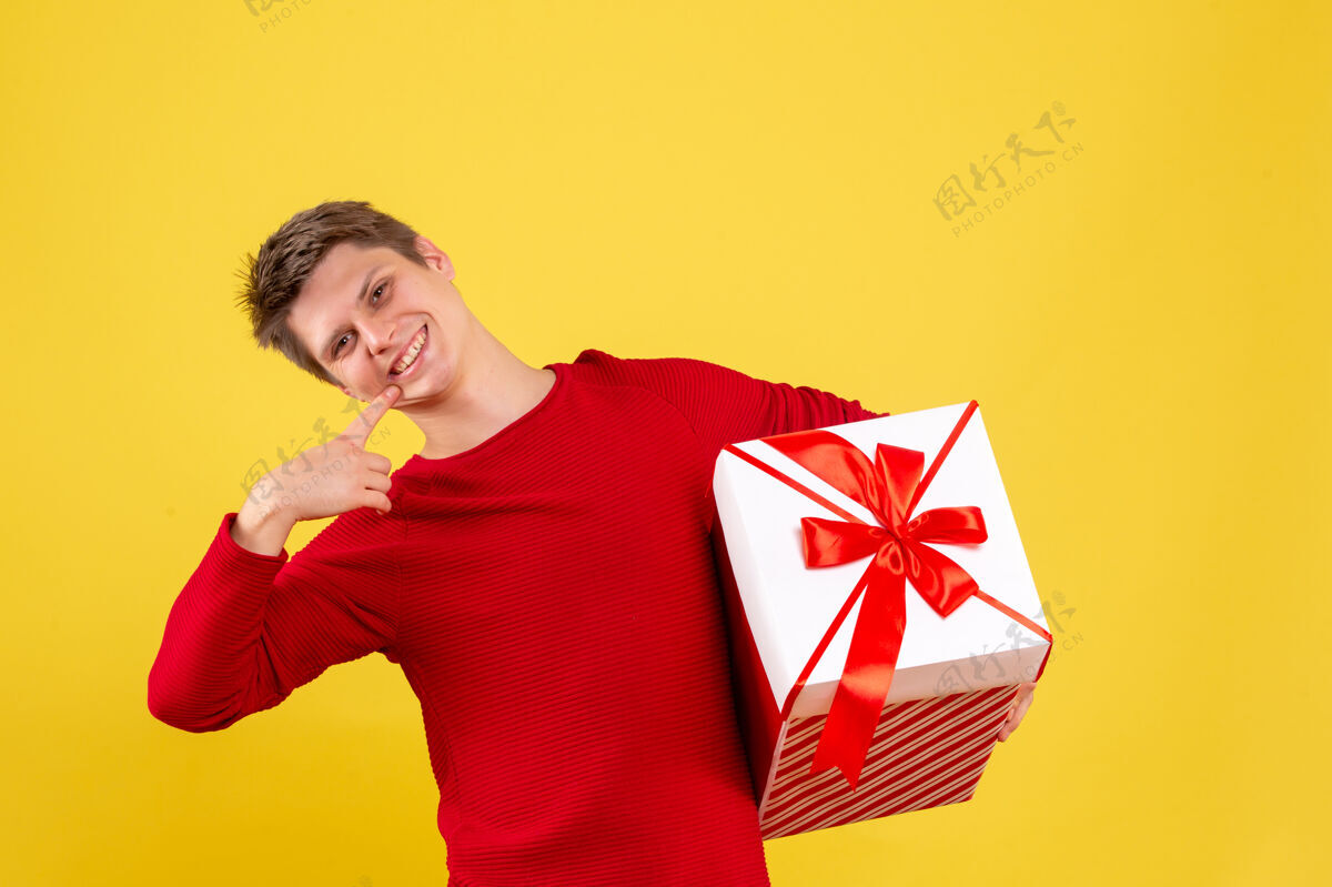 大正面图黄色背景上有大圣诞礼物的年轻男性圣诞年轻男性微笑