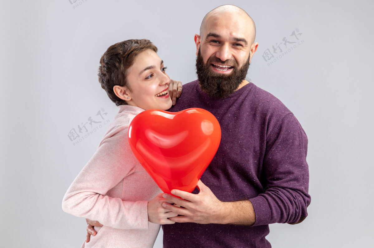 微笑一对穿着休闲服的年轻夫妇手持心形气球 站在白色背景上欢笑着欢庆情人节休闲年轻情侣
