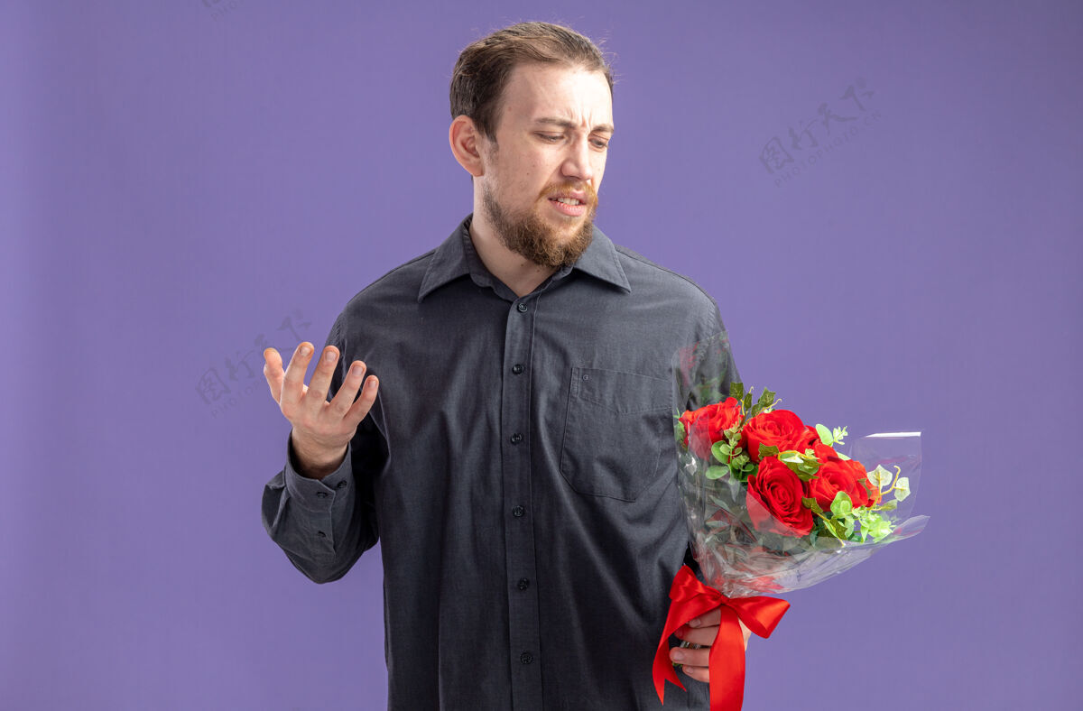 男人一个穿着休闲服的年轻人拿着一束红玫瑰为女友看着 困惑地站在紫色背景下过情人节概念年轻困惑