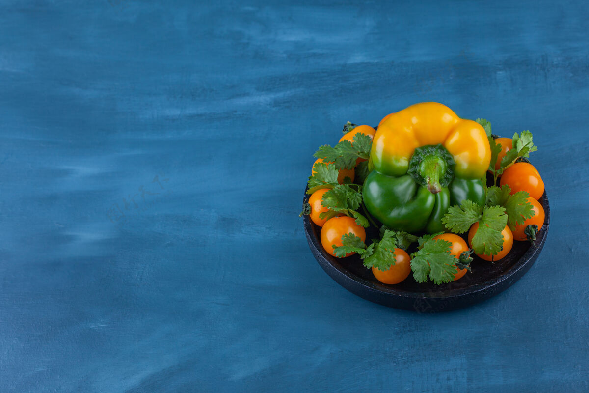 成熟的一盘黑甜椒和樱桃番茄放在蓝色的盘子里番茄有机铃铛