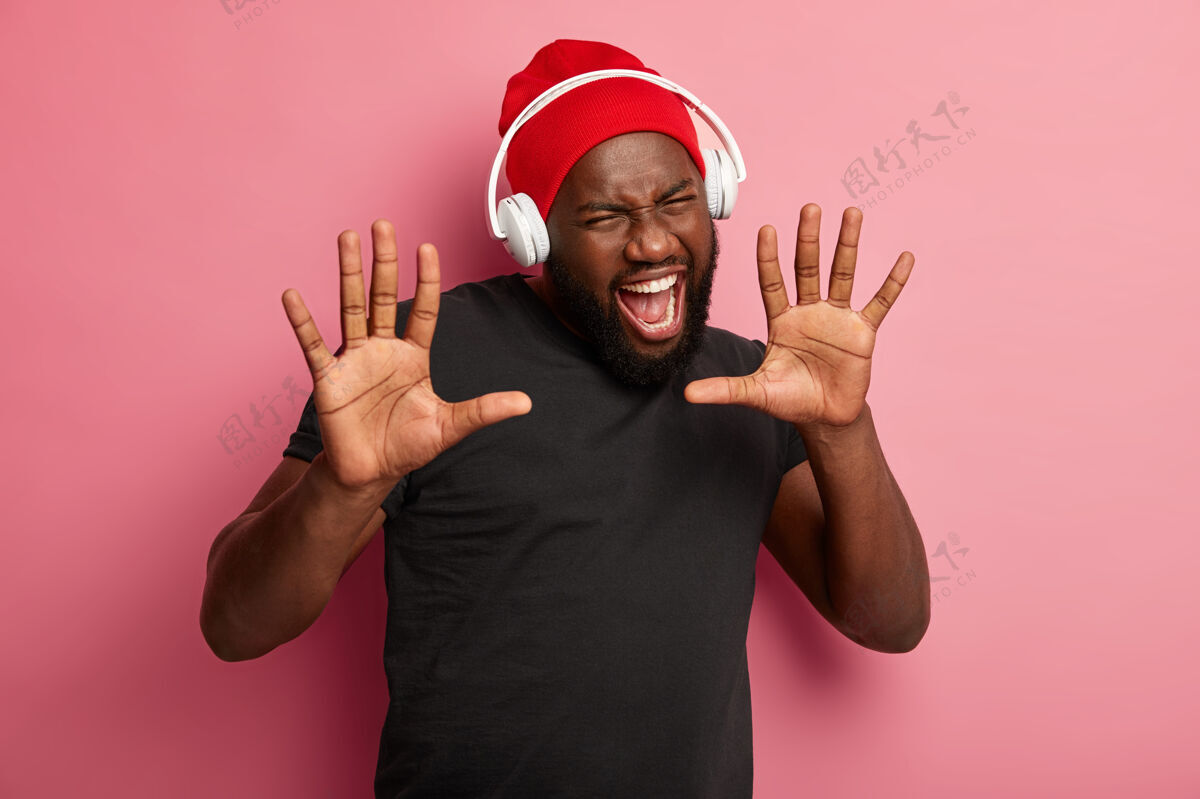 拍摄非裔美国人手掌向前 张大嘴巴 戴着红帽子和黑t恤 高兴地大叫 戴着耳机欣赏音乐音乐手掌头发