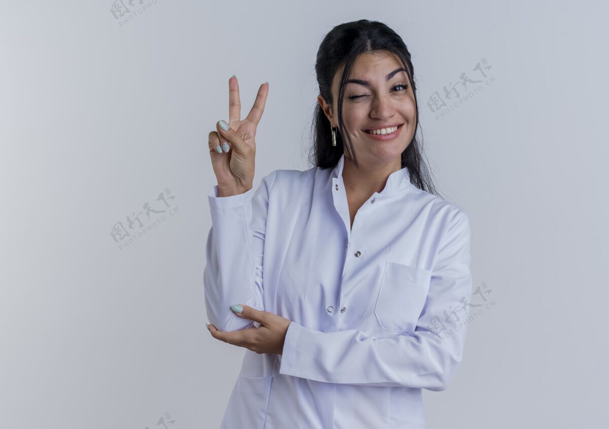穿面带微笑的年轻女医生穿着医疗袍 手放在手肘上做着和平的手势 隔离在白色墙壁上 留有复印空间看和平放