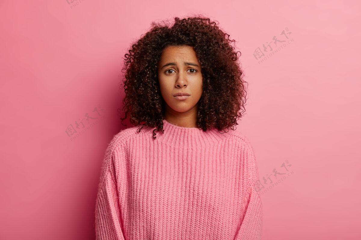 女性非洲女人有遗憾的表情 不高兴的表情 穿着休闲服 对坏消息不高兴 悲伤地看着镜头 穿着毛衣 孤立在粉色背景上女人青少年衣服