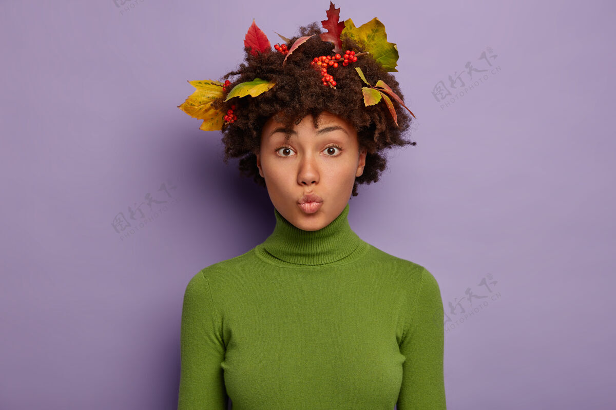 成人美丽的女人嘴唇圆润 留着短发 留着秋叶 穿着绿色高领毛衣 在紫色的背景下摆姿势圆形发型水平