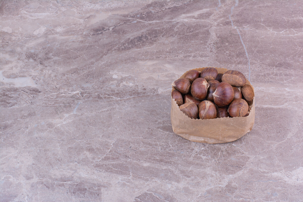 秋季棕色的栗子放在石头上的纸篓里异国情调食物酸味
