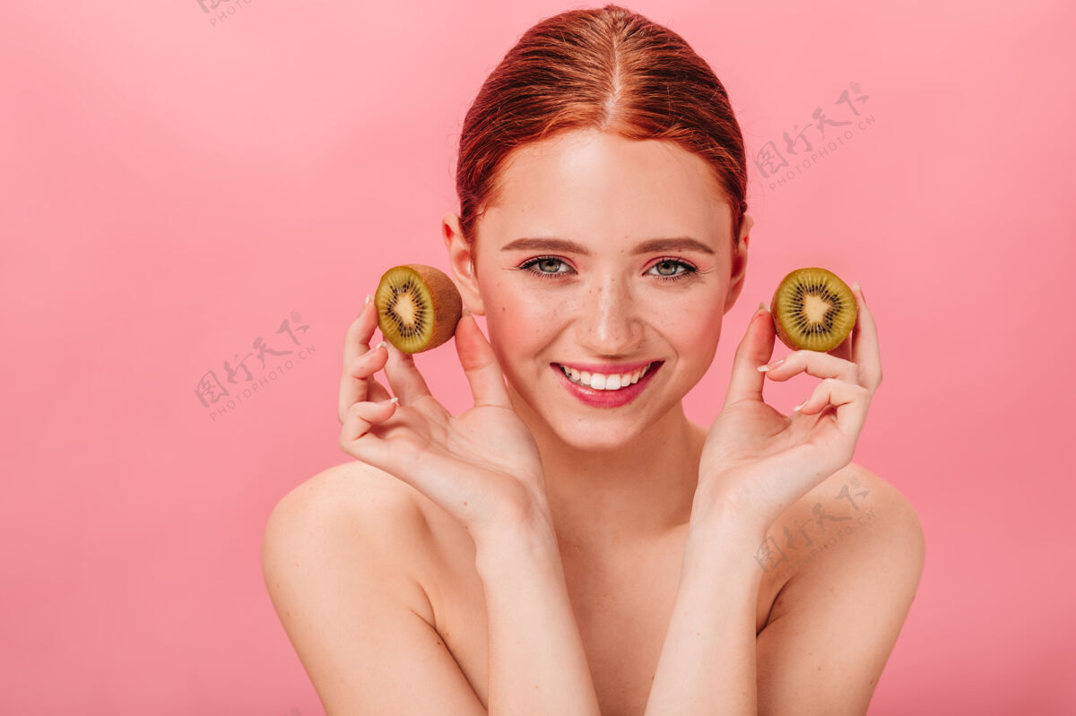 年轻人欢快的女孩和成熟的猕猴桃的正面视图姜女人与热带水果隔离在粉红色背景上的摄影棚拍摄脸裸体甜美