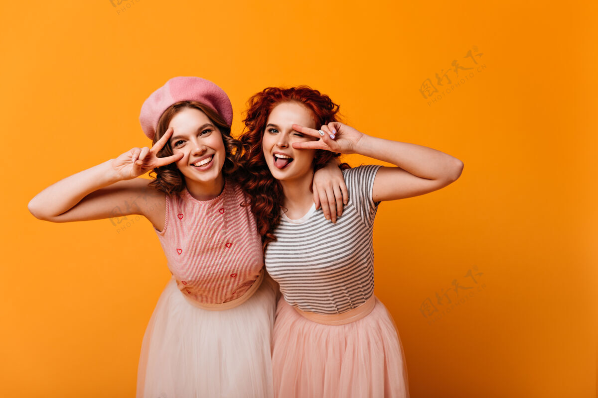休闲很高兴最好的朋友与和平标志合影摄影棚拍摄的穿着时髦服装的白人女孩在黄色背景下做手势情感表情两个人