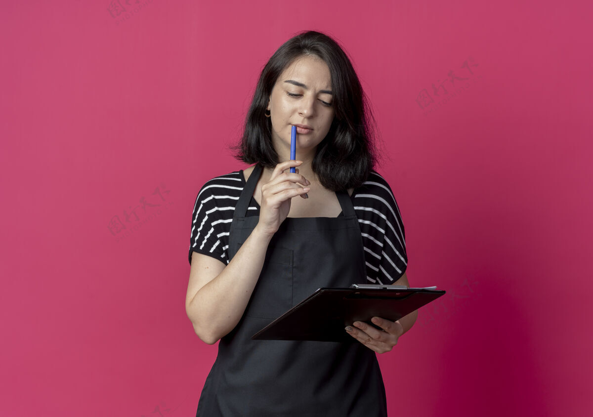 围裙年轻漂亮的女理发师围着围裙拿着写字板用钢笔看着它迷惑不解的粉色理发师拼图钢笔
