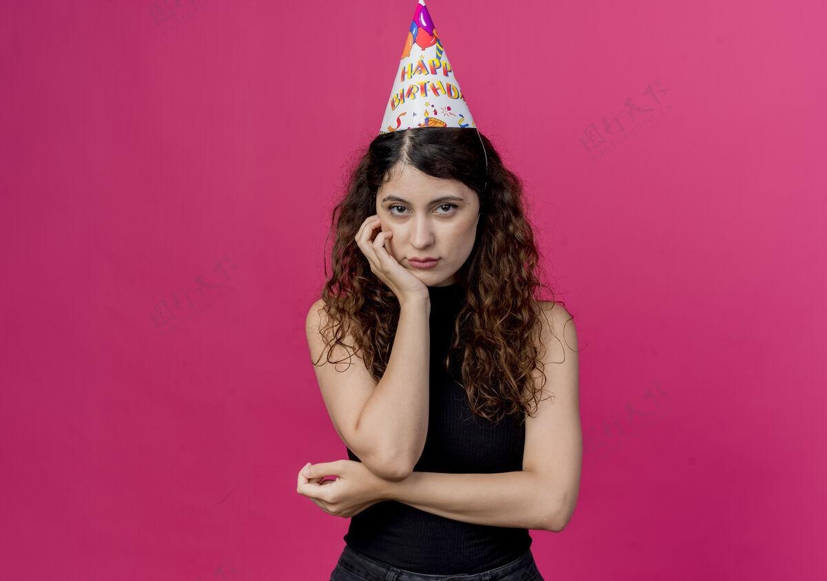 节日年轻漂亮的女士 卷发 戴着节日帽 脸上带着悲伤的表情 生日派对概念超过粉色表情女人卷发