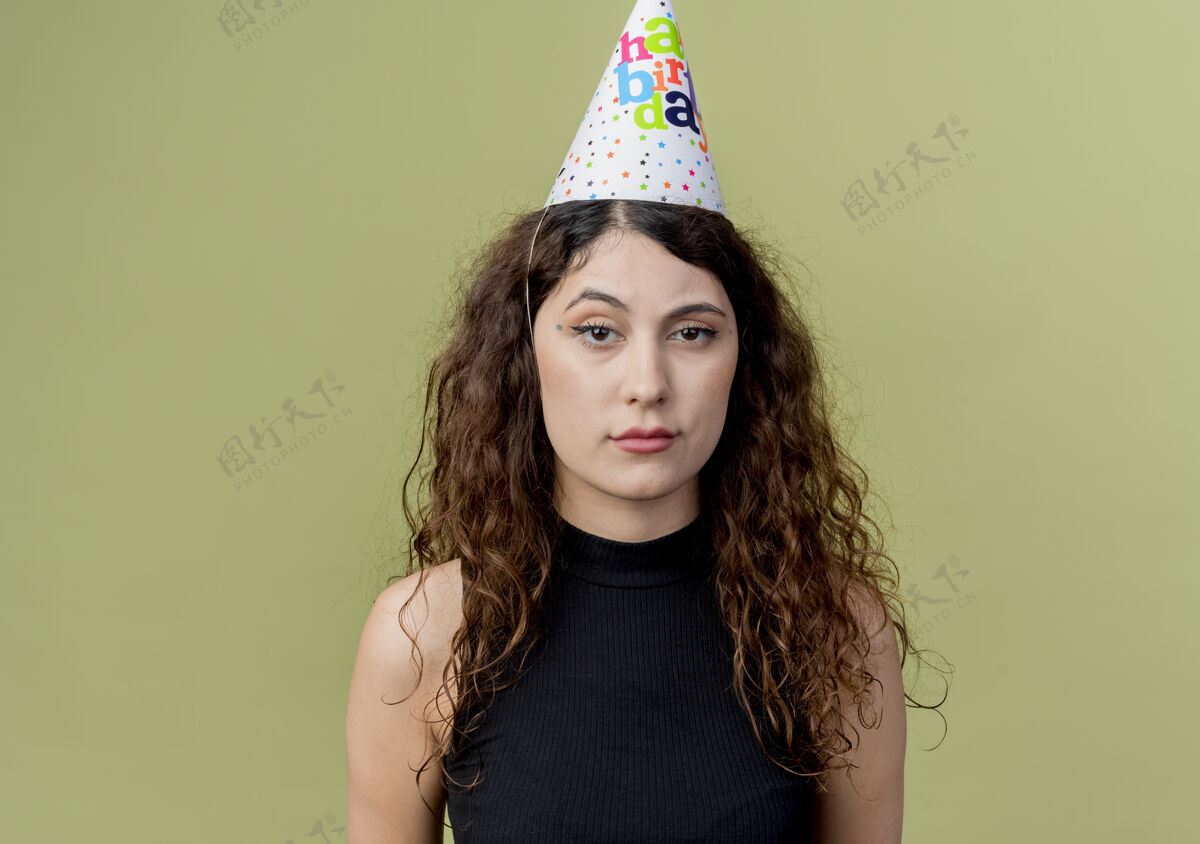 帽子年轻漂亮的女人 卷发 戴着节日帽 悲伤的表情 生日派对的概念 在灯光下聚会女人年轻