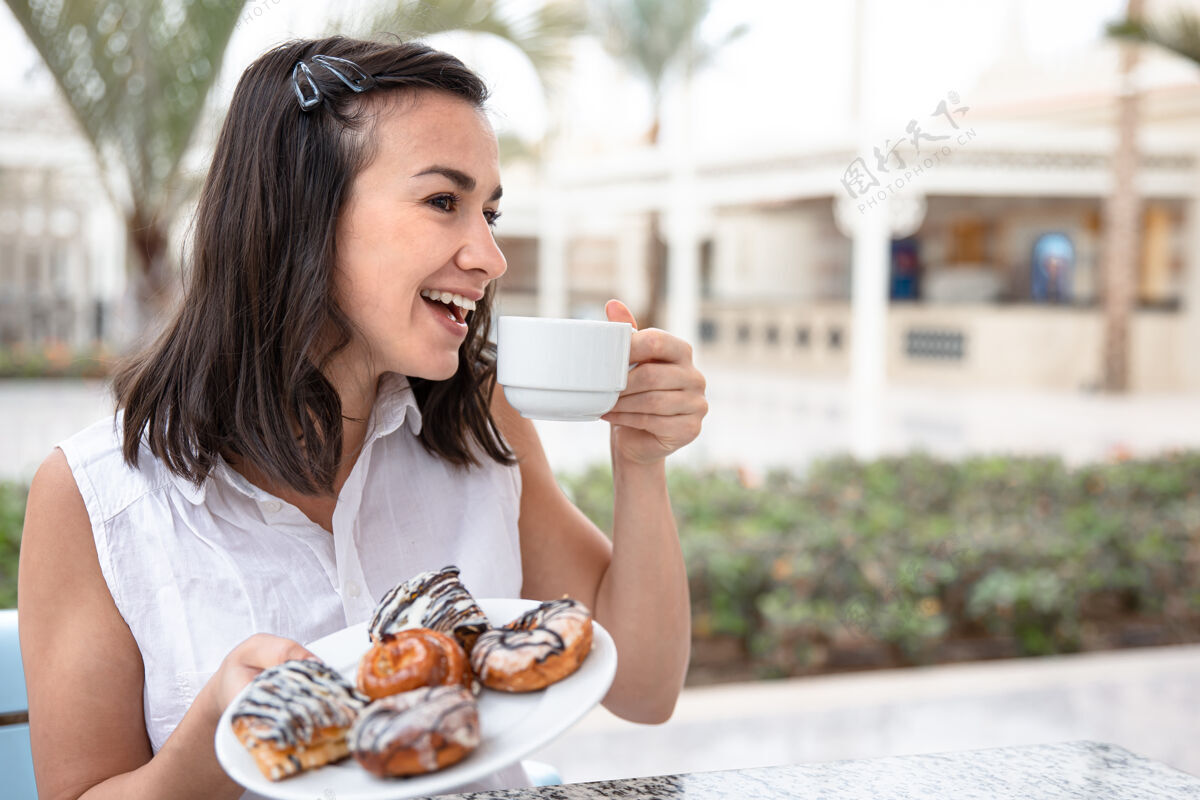 甜点快乐的年轻女子在户外露台上享受着早晨的咖啡和甜甜圈享受早晨饮料