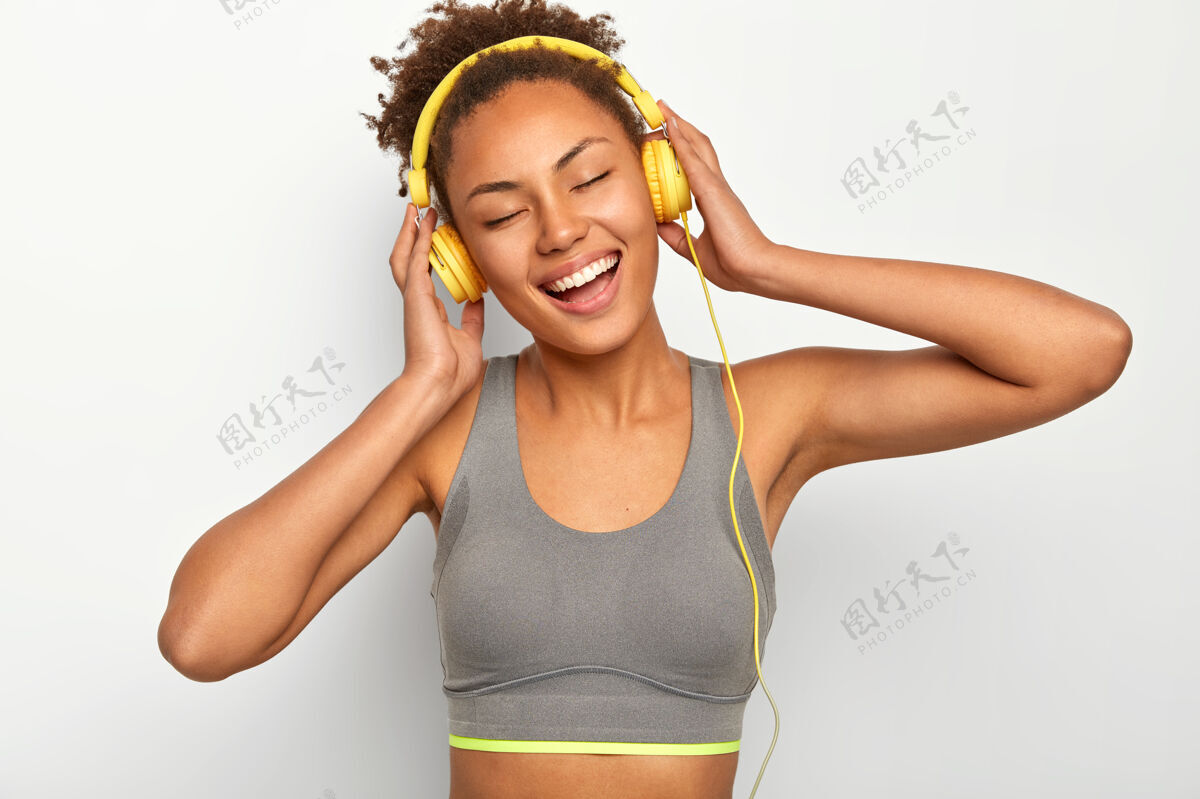 运动员情绪化的卷发美女 开怀大笑 戴着耳机享受着高亢的音乐 闭着眼睛不去享受快乐笑运动享受