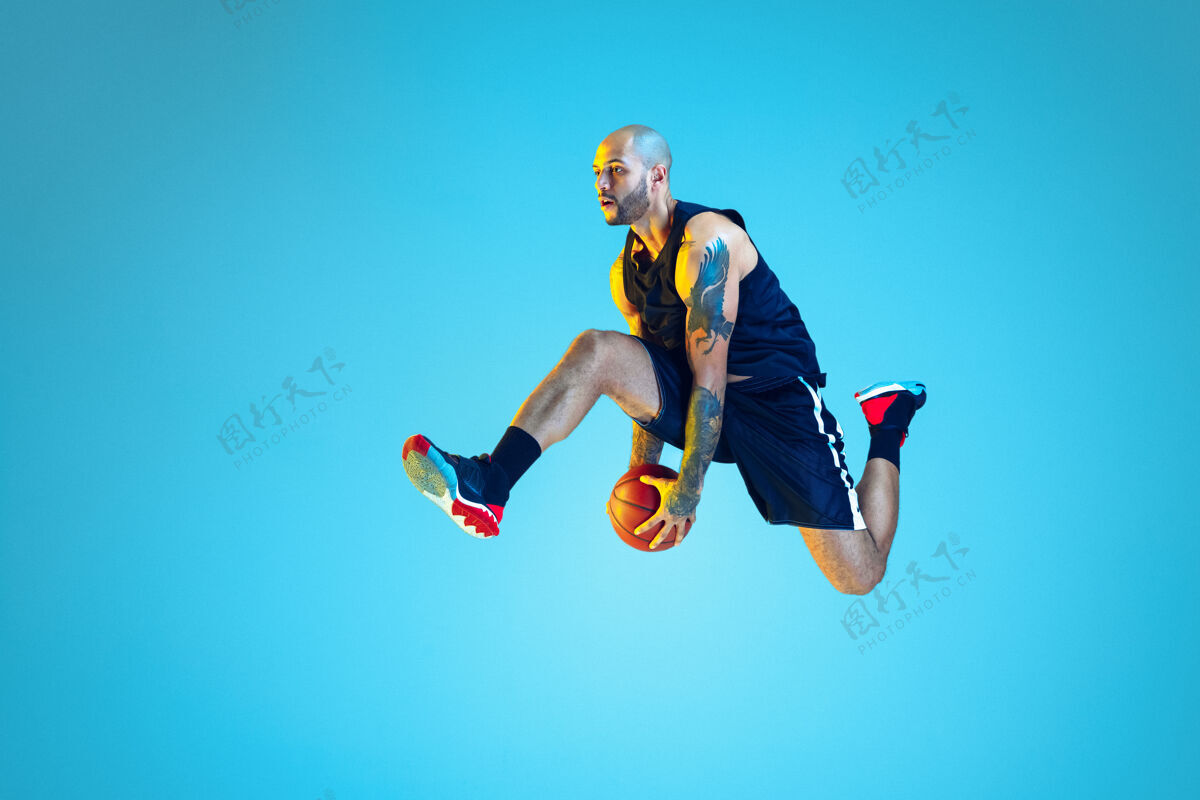 运动在跳跃中年轻的篮球队员穿着运动服训练 在运动中练习 在霓虹灯下在蓝色的墙上运动运动的概念 运动 活力和活力 健康的生活方式球场运动健身房