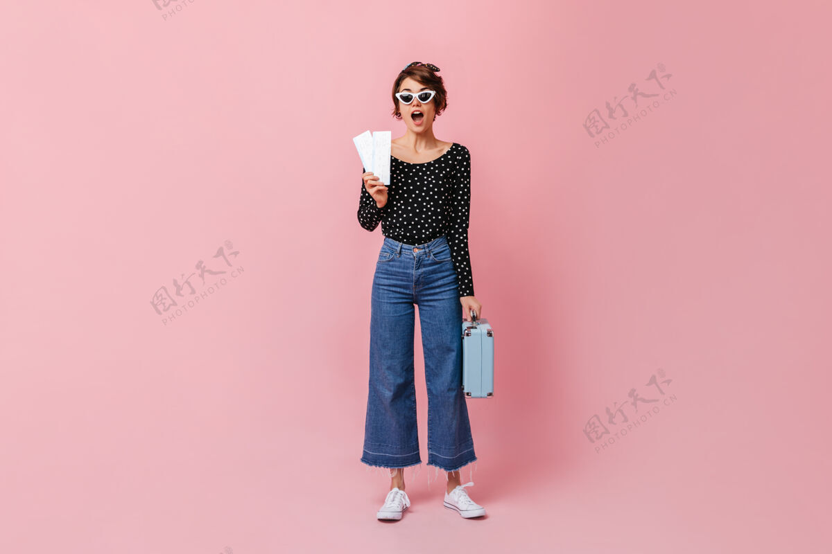 复制空间一个穿着牛仔裤的女人在粉红色的墙上拿着票休闲肖像年轻