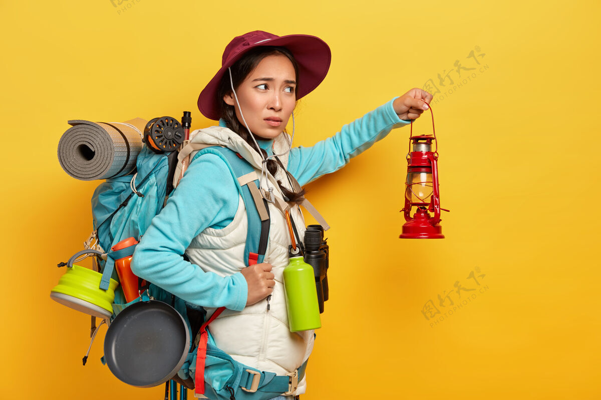 旅行不满的混血女背包客戴着时髦的帽子和暖和的背心 拿着煤油灯在黑暗中探索周围的环境散步女人姿势