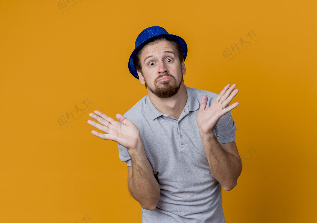 生日一个戴着帽子的年轻人在庆祝生日聚会上看起来很困惑 他把手臂伸向橙色的两边摊困惑壁板